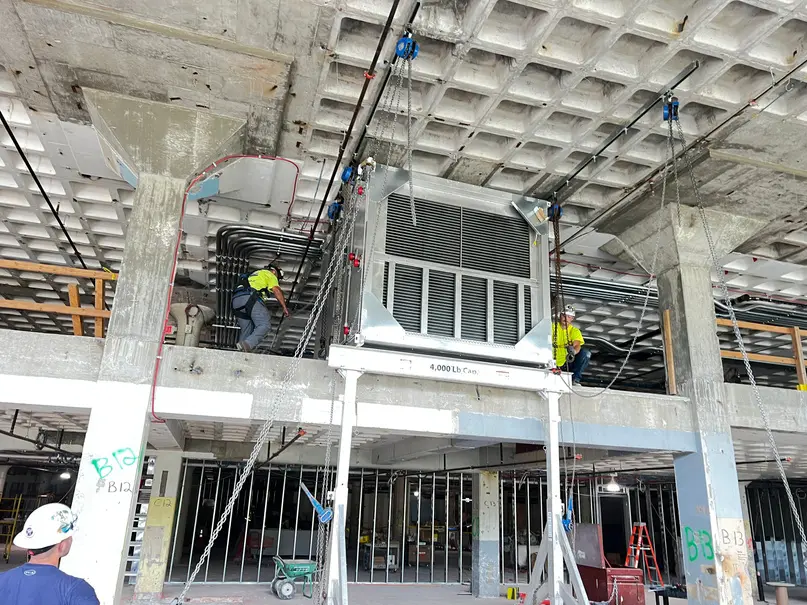 Riggers using a portable gantry to set an air handling unit inside a building under construction